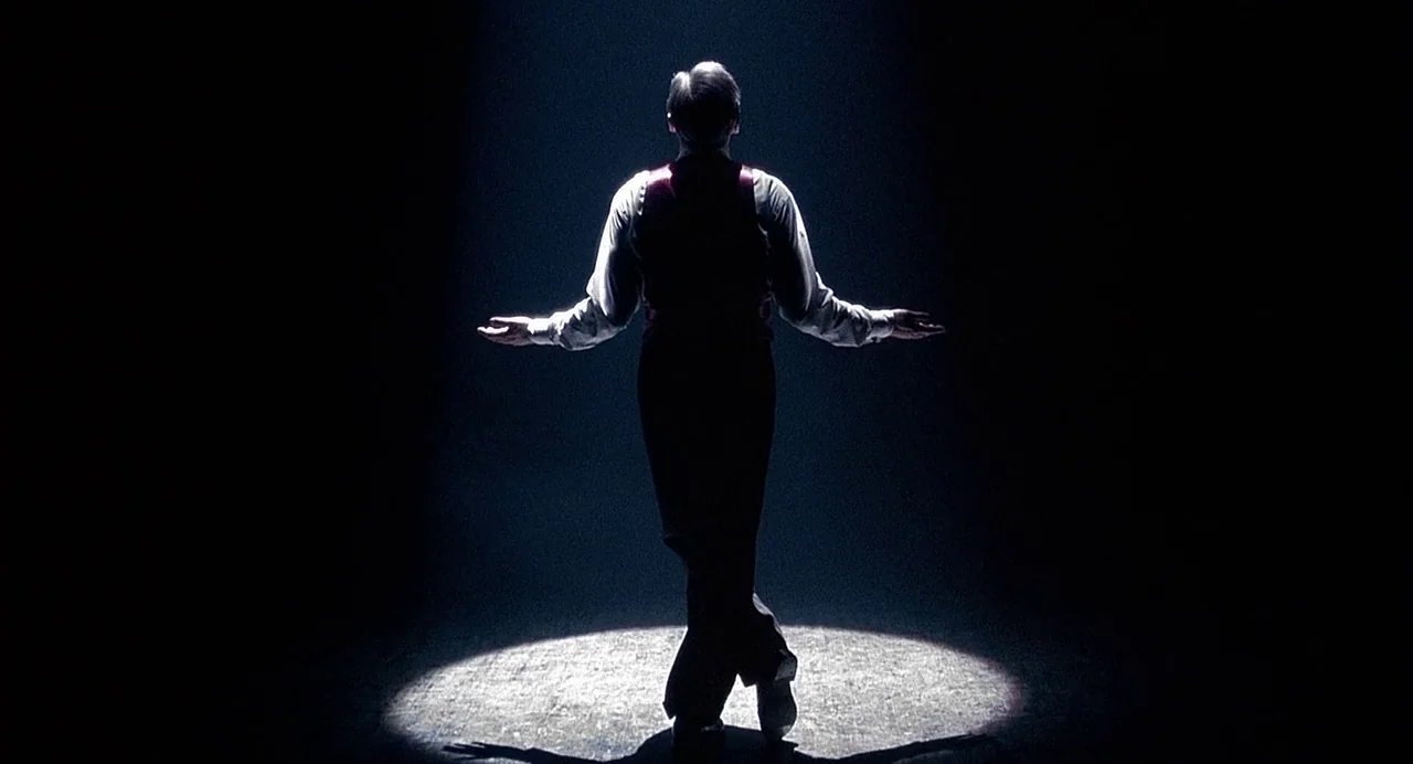 Chicago (2002) movie still: fullbody — A dark empty space is illuminated by a single focused overhead spotlight. A man in formal attire stands in…