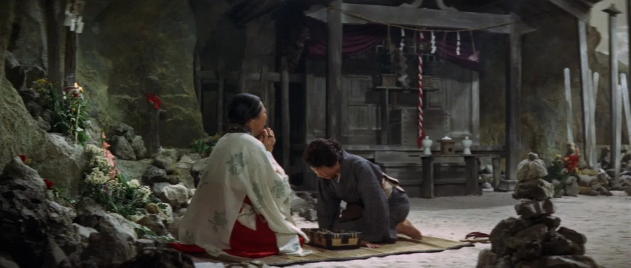 Ebirah Horror of the Deep (1966) movie still: wide — A stone cavern features a small wooden shrine tucked into the rear wall. Two women kneel on a…