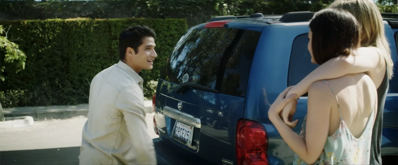 Truth or Dare (2018) movie still: medium — A sunny parking lot features a blue SUV with a green hedge in background. A man smiles as he walks toward…