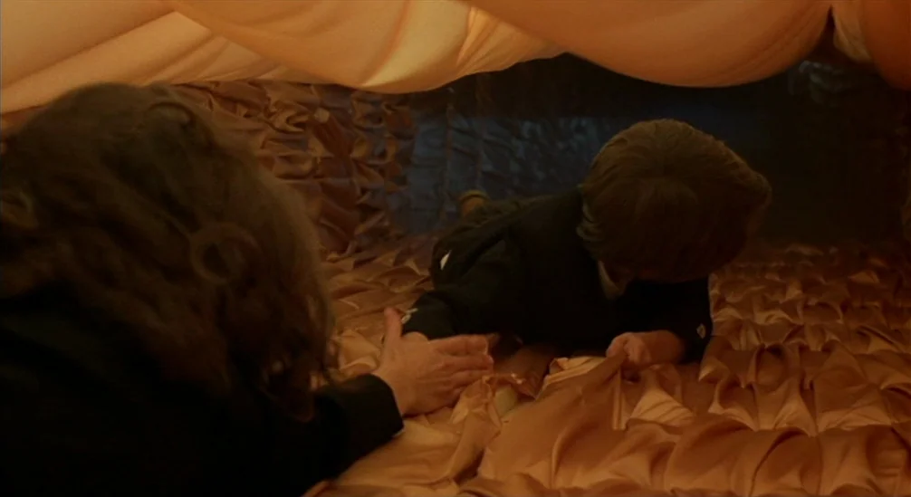 New Nightmare (1994) movie still: medium — A person reaches inside a constricted tunnel constructed from gathered peach-colored fabric. A small…