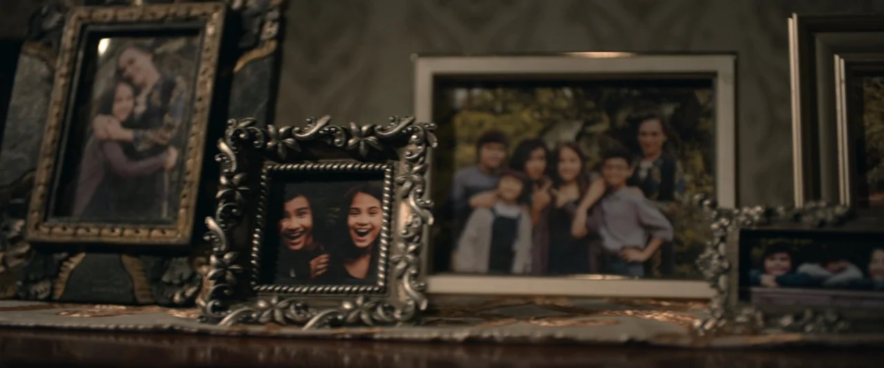 The Chanting 3 (2008) movie still: medium — A dark wooden mantelpiece holds several framed family photographs arranged in a row. The images are…