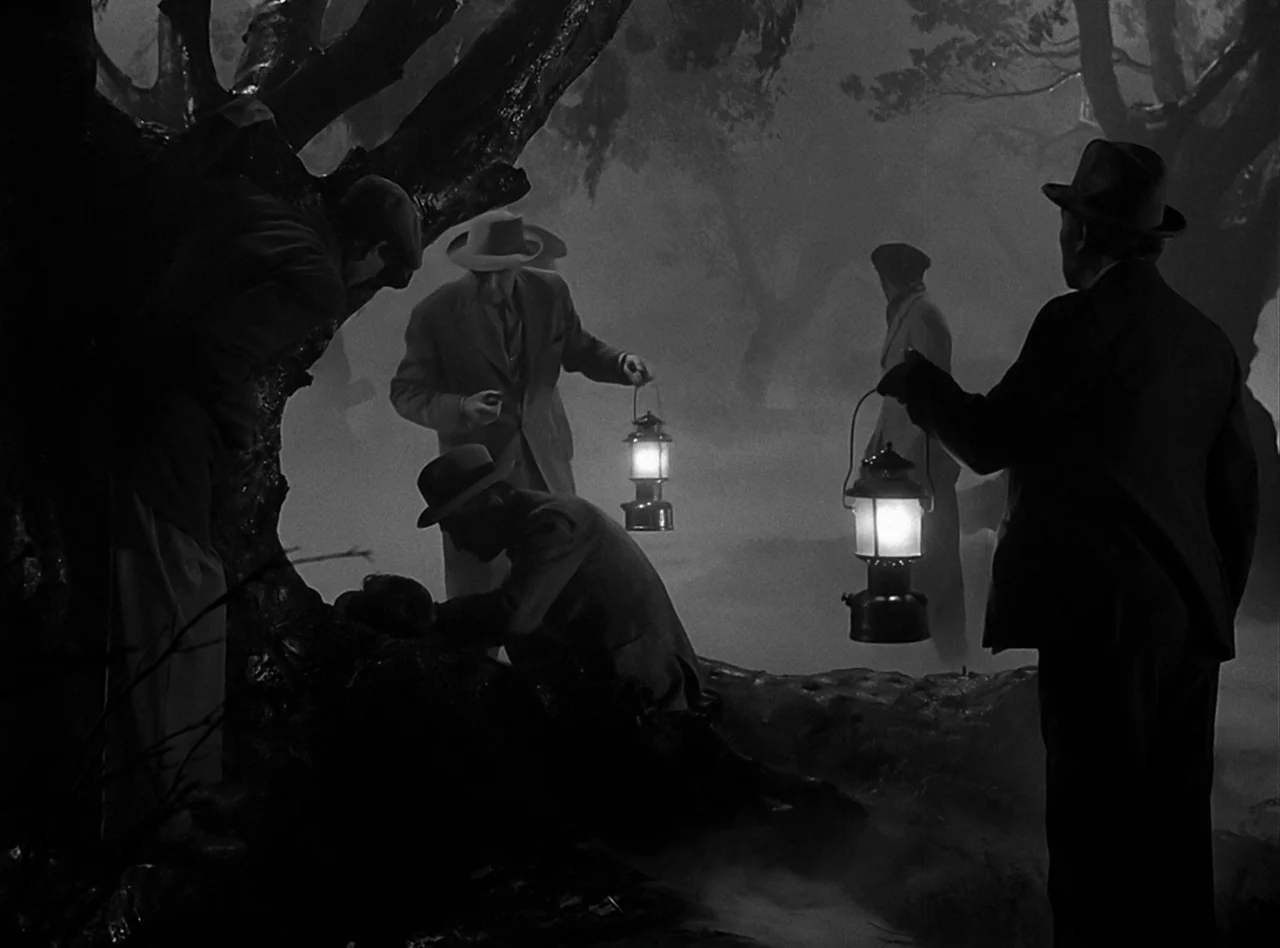 The Wolf Man (1941) movie still: wide — A dark, foggy wooded area with large, gnarled trees obscuring the deep background. Several men in 1940s…