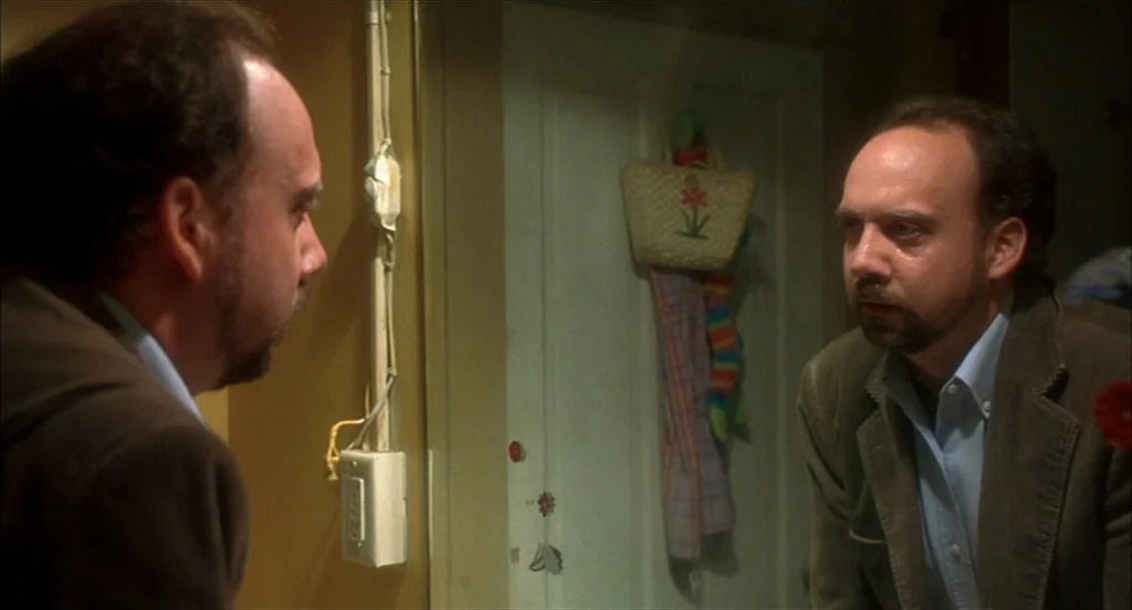 Sideways (2004) movie still: medium — A dimly lit residential bathroom features yellow walls and a wall-mounted mirror. A man gazes directly at his…