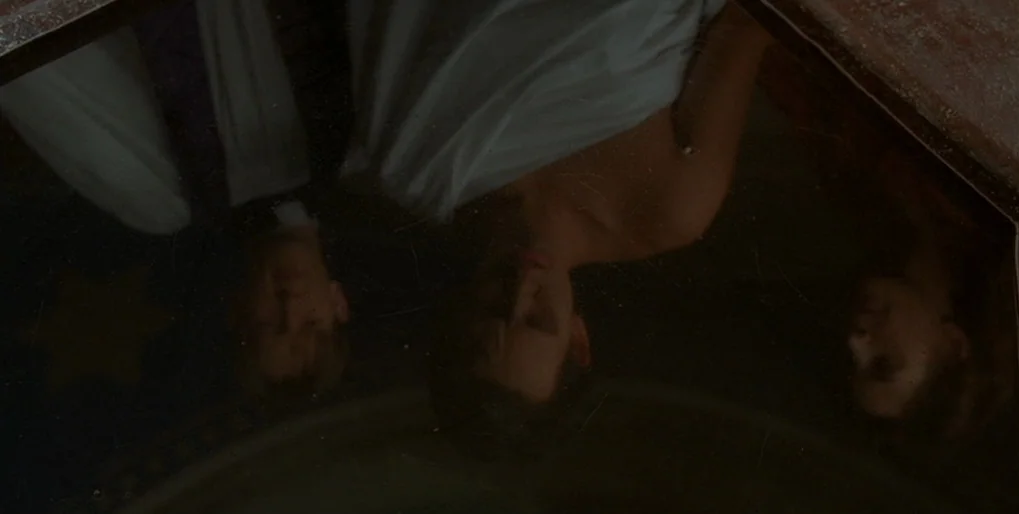 Dominion: Prequel to the Exorcist (2005) movie still: medium — Three people are reflected looking down into a dark, glossy, possibly circular…