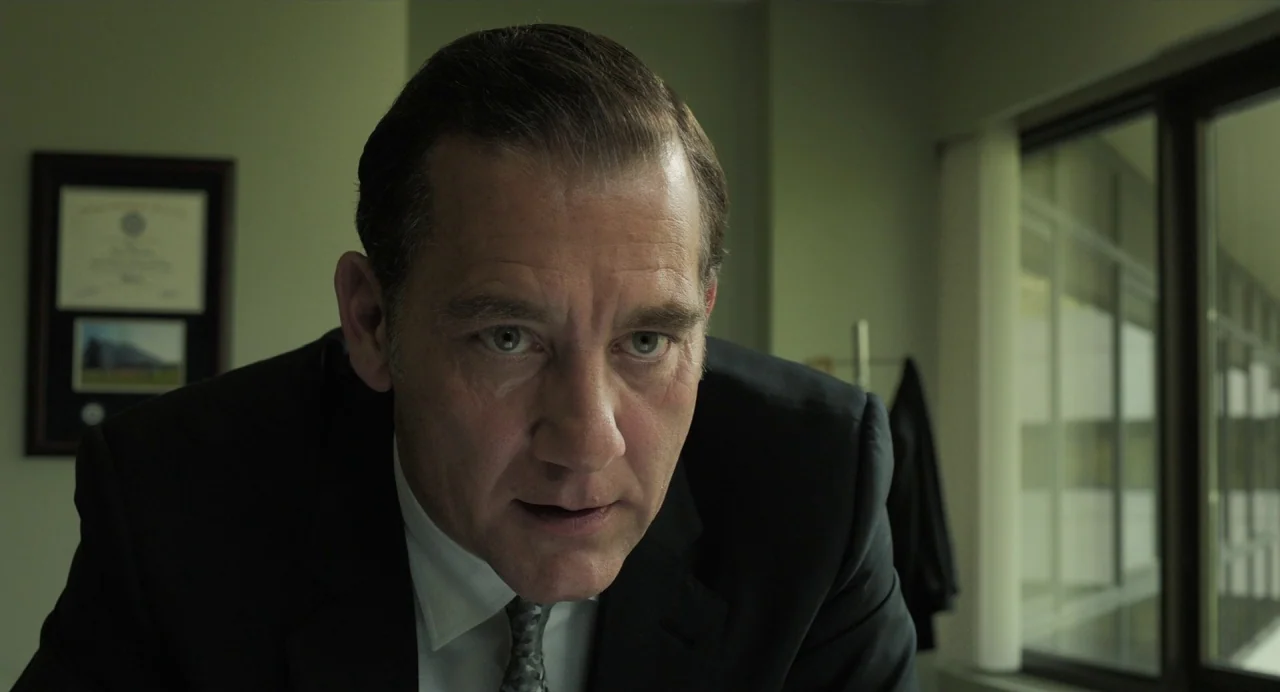 Gemini Man (2019) movie still: closeup — An office interior features beige walls, a framed certificate, and large windows. A middle-aged man in a…
