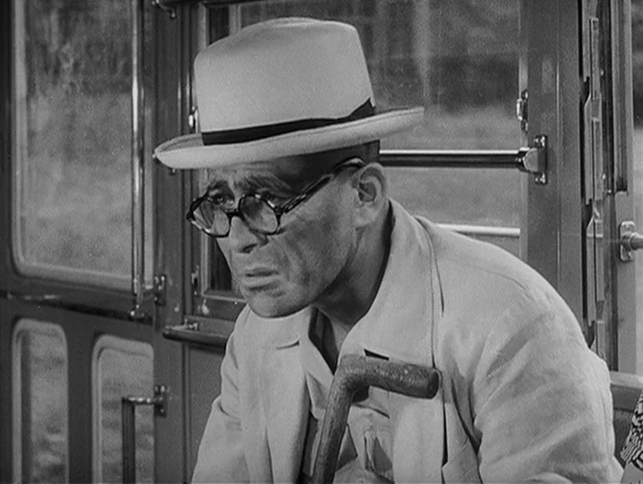 I Live In Fear (1955) movie still: medium — A man sits inside a vintage passenger train compartment with wood-paneled walls and windows. He is…