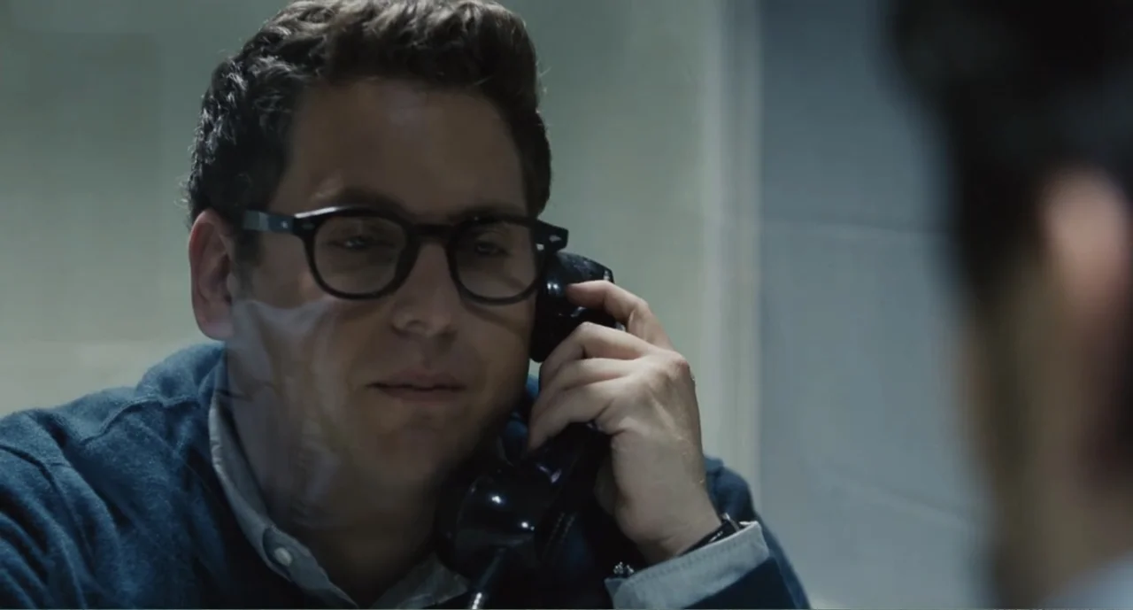 Bad Boys: A True Story (2003) movie still: closeup — A spartan visiting room features a pane of glass and plain, light-colored walls. A man in a…