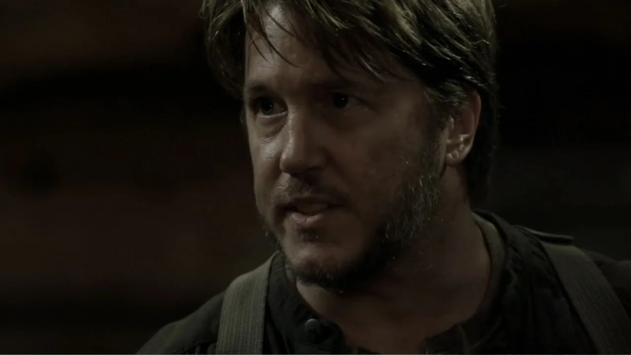 Dawn Rider (2012) movie still: closeup — A man in a dark environment is captured against a blurred, indistinct background. The man has short brown…