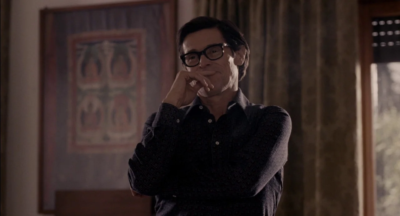 Pasolini (2014) movie still: medium — A residential room features a framed religious scroll on the wall behind the subject. A man stands wearing a…