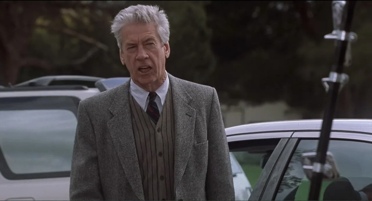 National Lampoon's Van Wilder (2002) movie still: medium — An outdoor parking lot with light-colored vehicles visible in the background. An older…