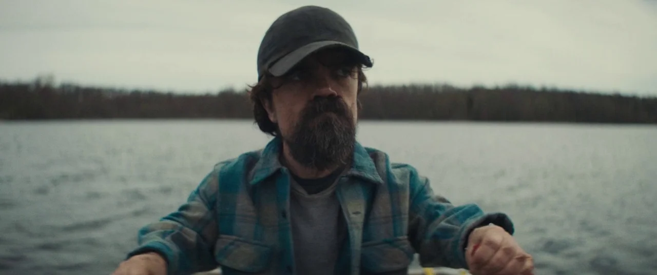I Think We’re Alone Now (2018) movie still: medium — A man rows a small boat across a wide lake under an overcast sky. The distant shoreline is…