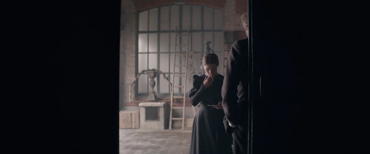 The Dancer movie still: wide — An industrial studio space features a large arched window with brick surrounds and ladders. A woman stands in the…