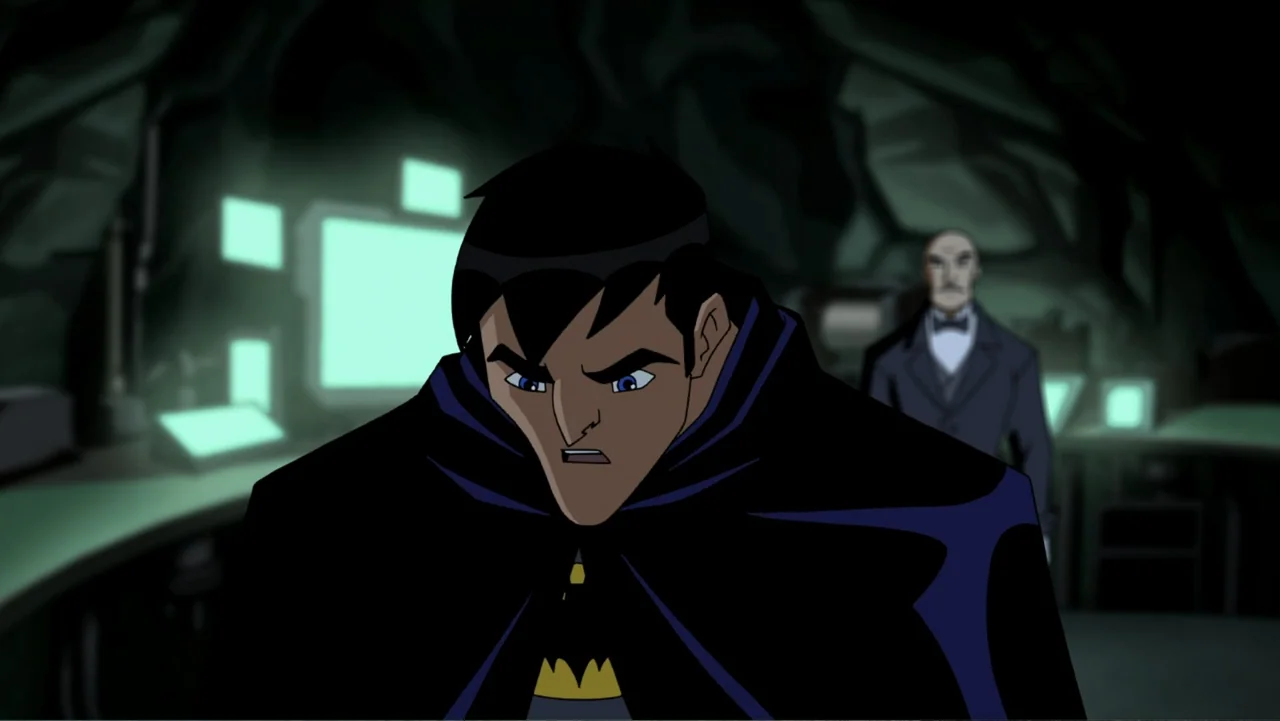 Batman: Year One (2011) movie still: medium — A dark subterranean space filled with glowing computer screens and rocky cave walls. A caped man…