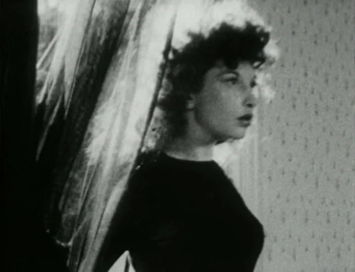 Meshes of the Afternoon (1943) movie still: medium — A woman stands near a window inside a room with patterned wallpaper. She turns her head…