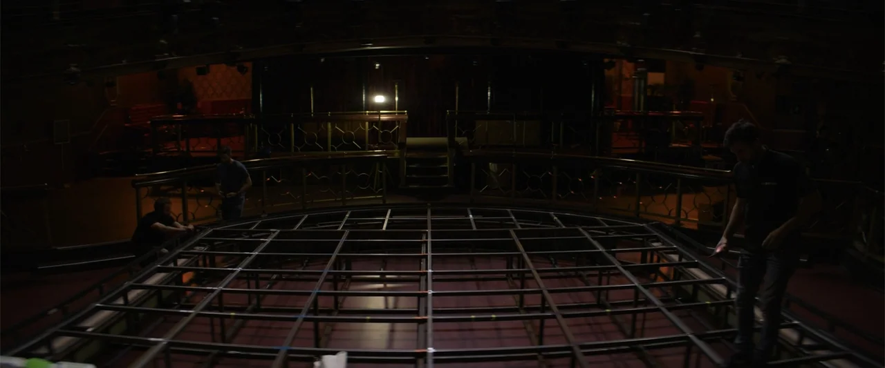 Magic Mike's Last Dance (2023) movie still: wide — A large, dark music hall interior features a central metal grid platform under construction.…