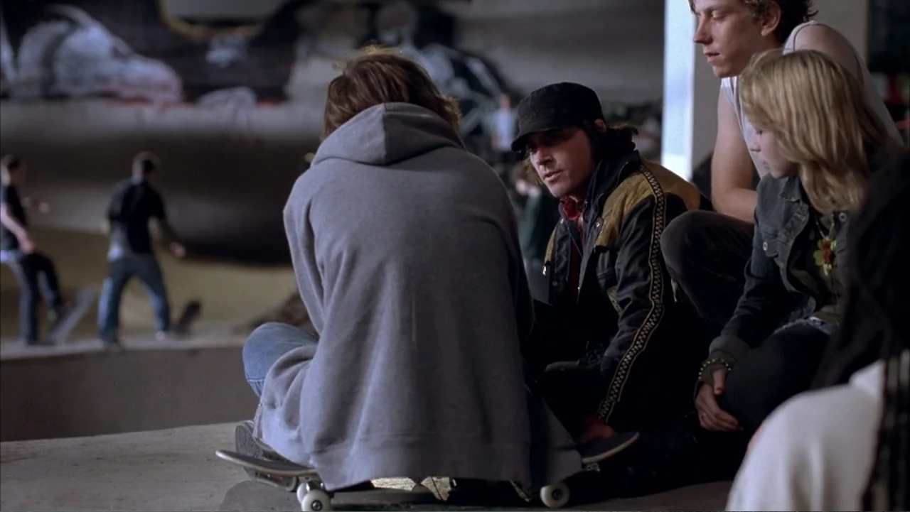 Paranoid Park (2007) movie still: medium — A group of young people gather at the edge of a concrete indoor skatepark. The individuals sit on the…