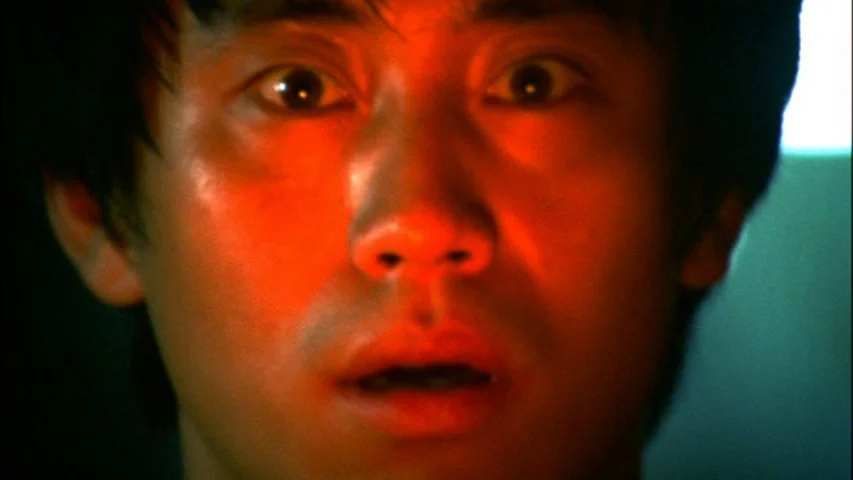 Save The Green Planet! (2003) movie still: closeup — An interior space is cast in shadows. A man's face is illuminated by a strong red light source.