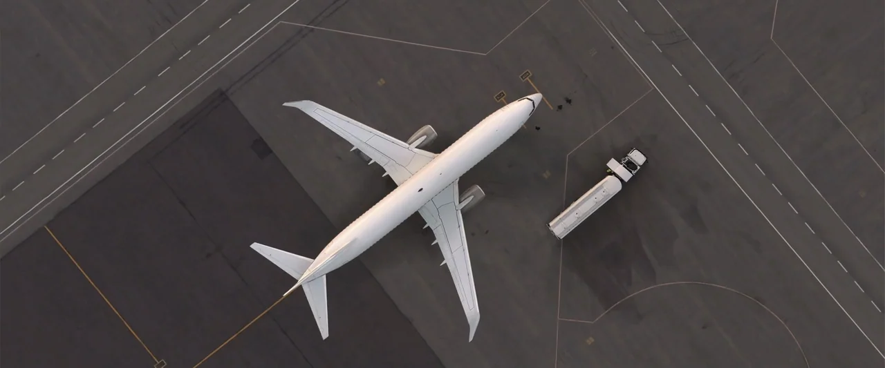 Operation Fortune: Ruse de Guerre (2023) movie still: establishing — An aerial view shows a large white passenger jet parked on a gray asphalt…