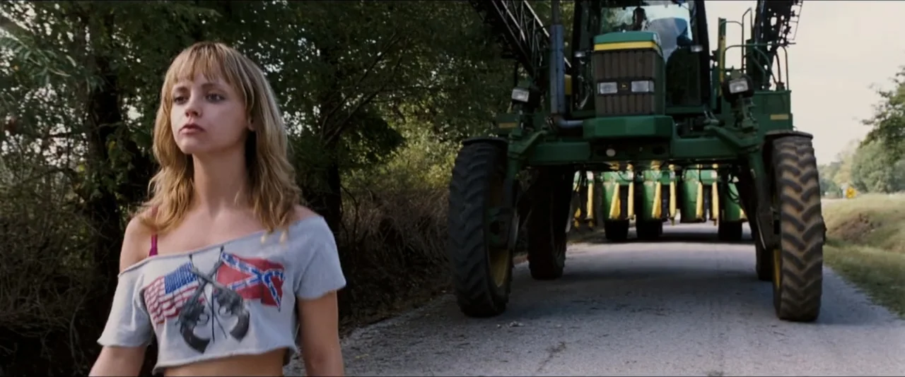 Black Snake Moan (2006) movie still: medium — A rural asphalt road passes through trees with a large green agricultural sprayer machine. A young…