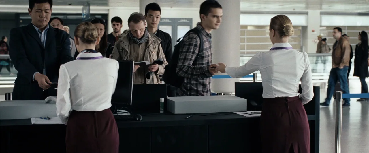Hector and the Search for Happiness (2014) movie still: medium — An airport check-in area features a long black desk with two staff members…