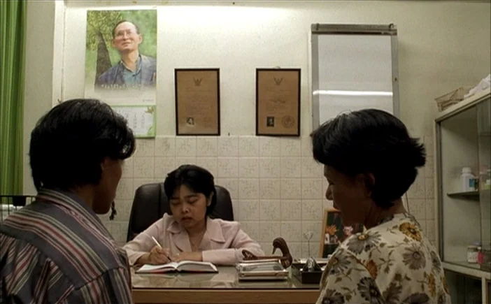 Blissfully Yours (2002) movie still: medium — A small, utilitarian office contains a desk and tiled walls decorated with framed certificates. A…