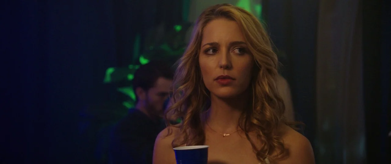 Happy Death Day (2017) movie still: medium — A dark indoor party setting with dim ambient lighting in shades of blue and green. A young woman with…