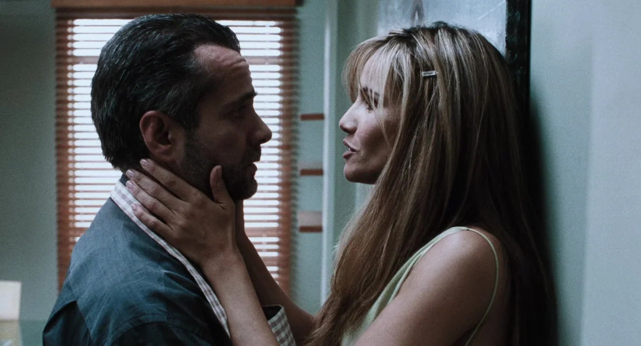 Amores Perros (2000) movie still: medium — A man and a woman stand face-to-face in a kitchen with window blinds visible. The woman holds the man's…