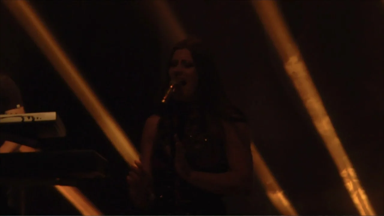 Soaring Highs and Brutal Lows: The Voices of Women in Metal (2015) movie still: medium — A dimly lit concert stage features a singer illuminated by…