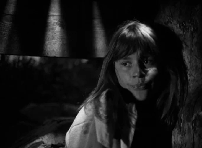 Summer with Monika (1953) movie still: closeup — A dimly lit interior space with shadows cast across a textured wall. A teenage girl looks toward…