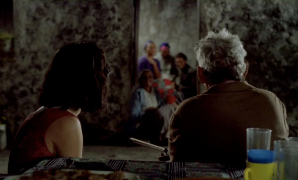 Casa De Lava (1994) movie still: medium — A dimly lit room with textured gray stone walls and a table in foreground. A man and a woman sit at the…