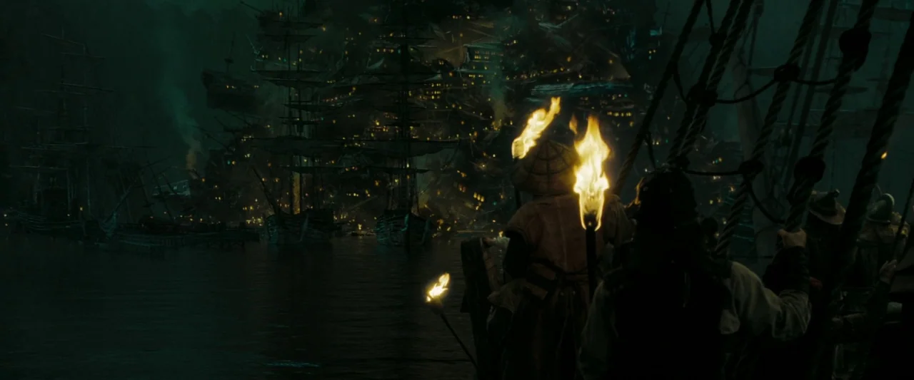 Pirates of the Caribbean: At World’s End movie still: wide — A dark, expansive harbor features numerous sailing ships docked before a towering, lit…