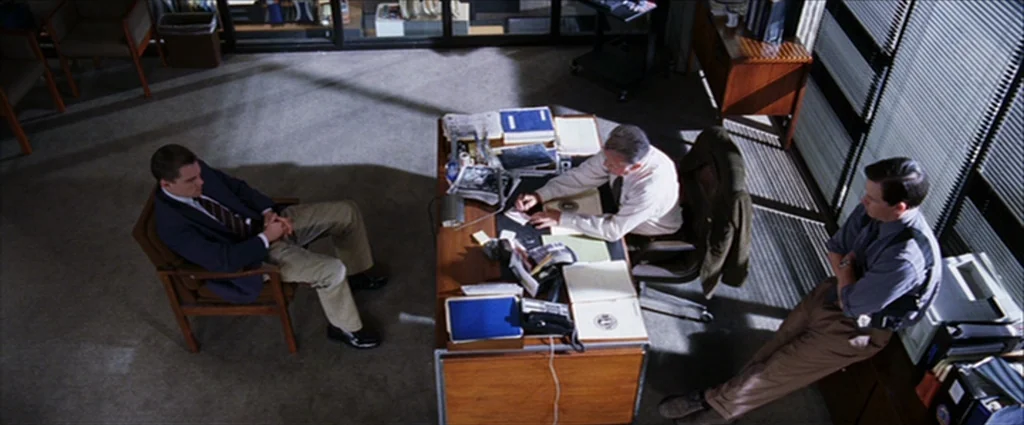 The Departed (2006) movie still: wide — A top-down view of a wood-paneled office with a large desk and file storage. One man sits in a chair while…