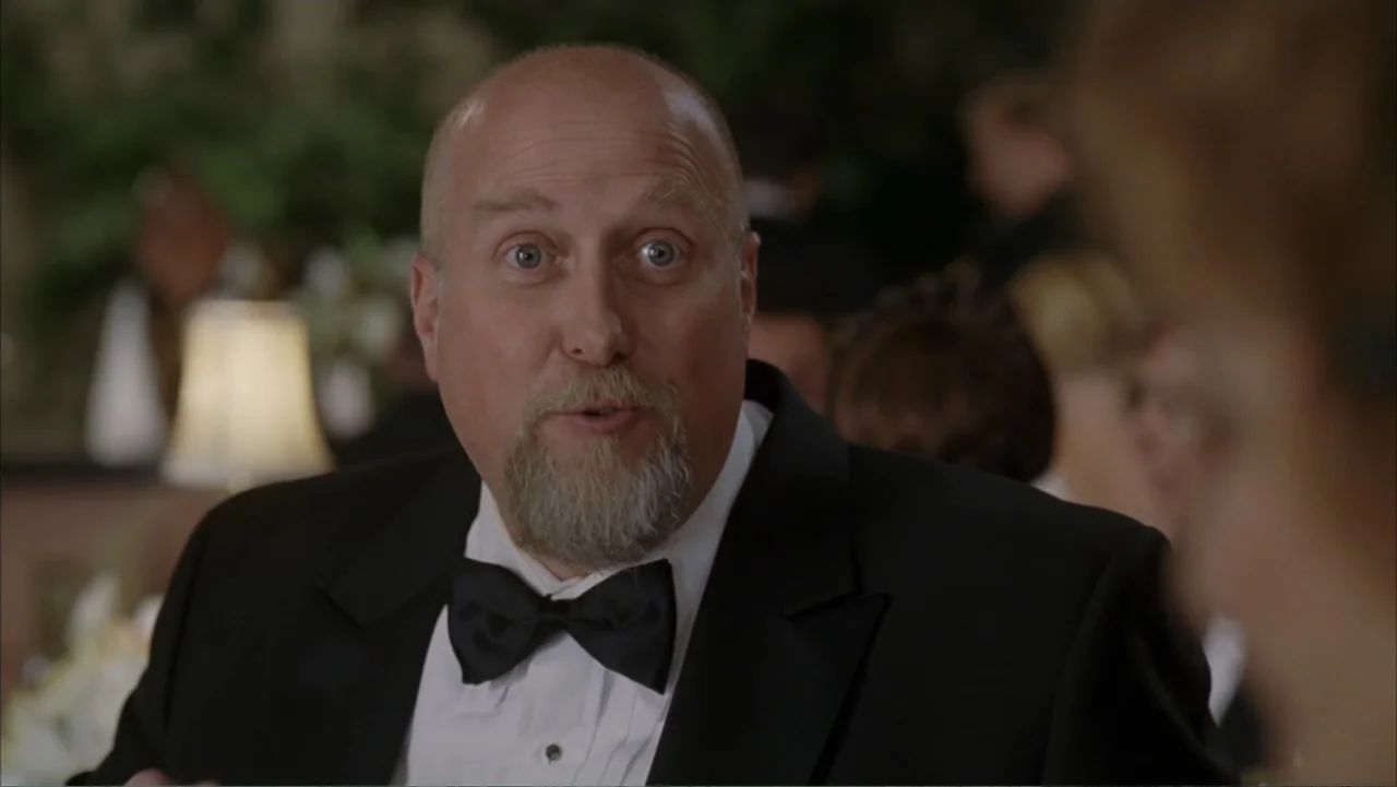 Rumor Has It... (2005) movie still: medium — A banquet hall at night with soft ambient light from room lamps. A middle-aged man in a tuxedo engages…
