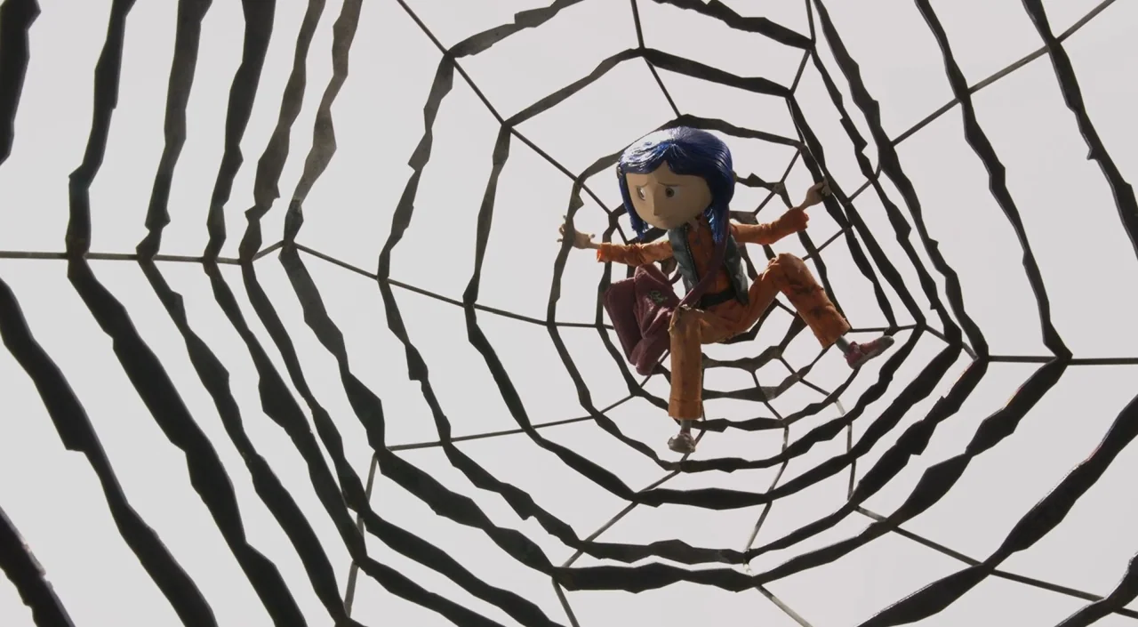 Coraline (2009) movie still: wide — A stylized, rigid spider web structure spans the frame against a pale, featureless background. A small doll-like…