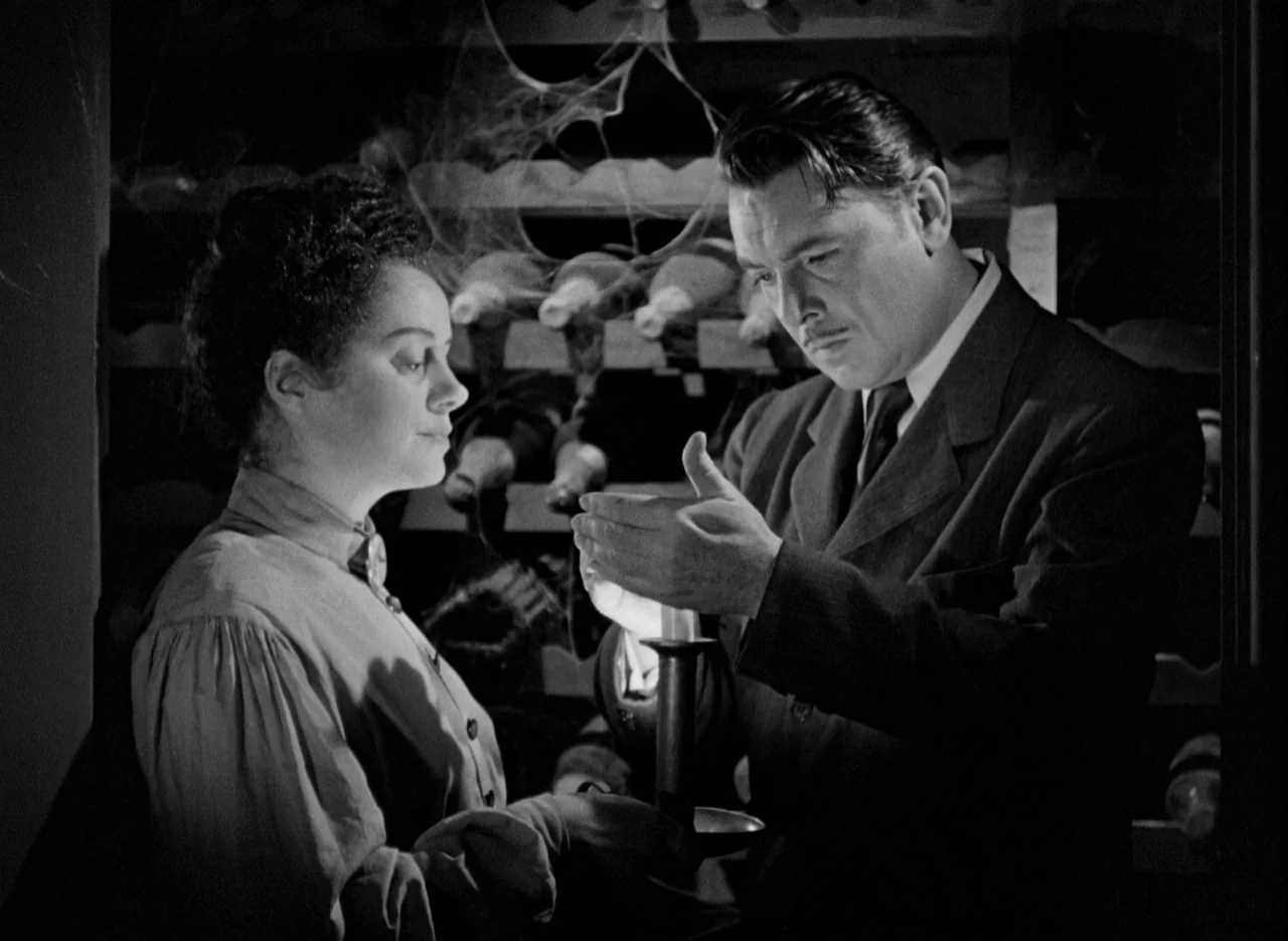 The Spiral Staircase (1946) movie still: medium — A dusty wine cellar features wooden racks filled with cobweb-covered glass bottles. A man and…