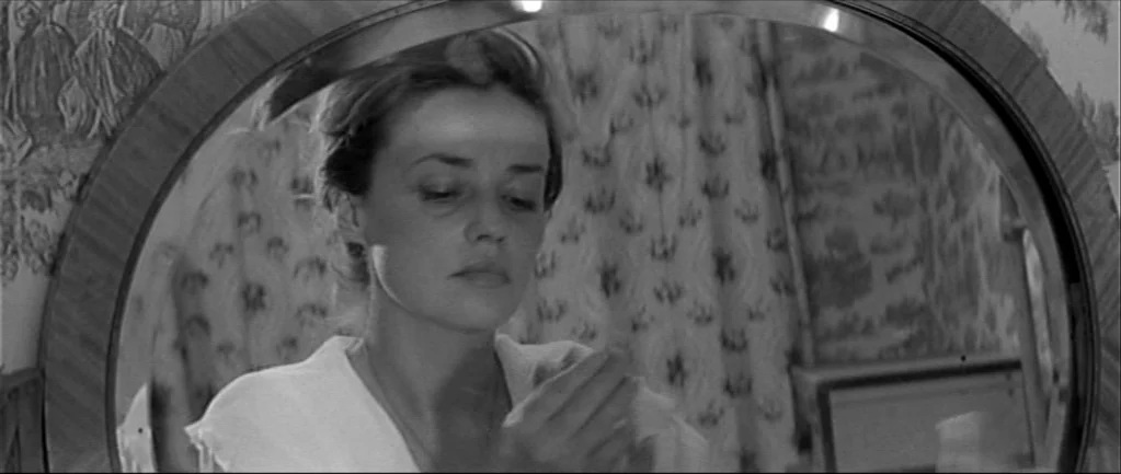 Jules and Jim (1962) movie still: closeup — The frame is filled by a circular mirror showing a reflection of a woman. Behind her, a floral patterned…