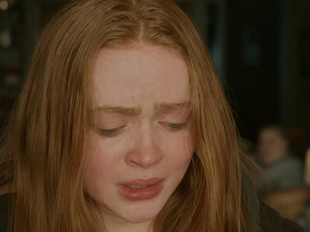 The Whale (2022) movie still: closeup — A close-up shot focuses on a young woman with long strawberry-blonde hair. She keeps her eyes cast downward…