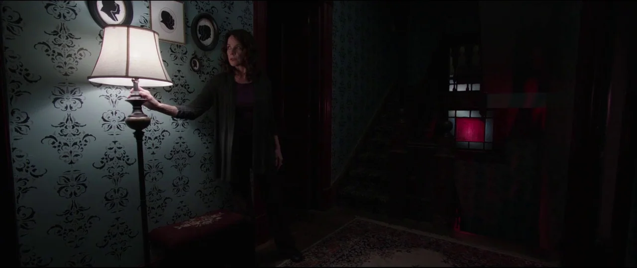 Insidious: Chapter 2 (2013) movie still: medium — A dark foyer features teal patterned wallpaper decorated with small framed silhouettes. A woman…