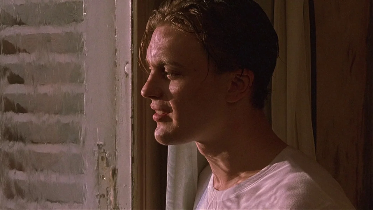The Dreamers (2003) movie still: closeup — An interior space features a man standing beside a shuttered window at night. The man gazes toward the…