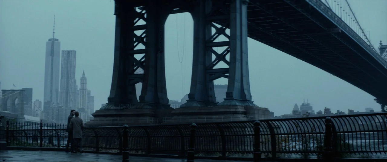 John Wick (2014) movie still: wide — A wet concrete promenade sits beneath the massive steel support pillars of a bridge. Two men stand by a black…