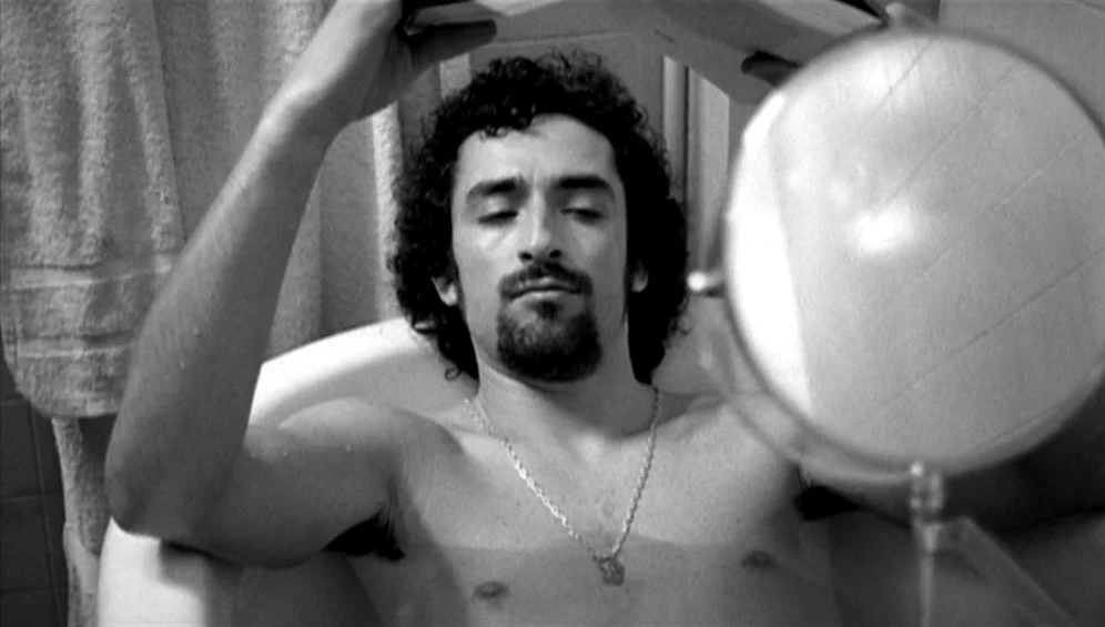 The Tango Lesson (1997) movie still: closeup — A man lies submerged in a white ceramic bathtub with a towel hung nearby. He holds a book open above…