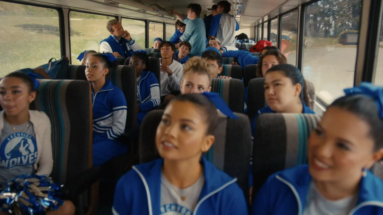 Sidelined: The QB and Me (2025) movie still: wide — The interior of a school bus is packed with high school students in uniforms. The students sit…