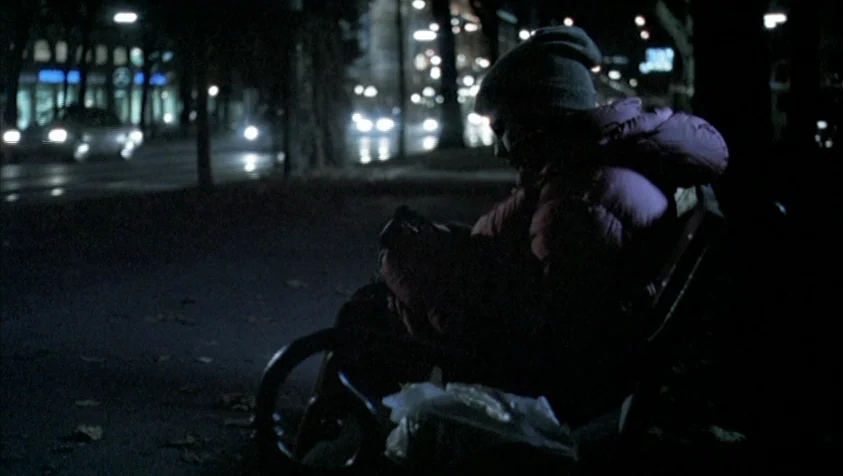 71 Fragments of a Chronology of Chance (1994) movie still: medium — A dark outdoor space at night with city traffic visible in the distance. A…