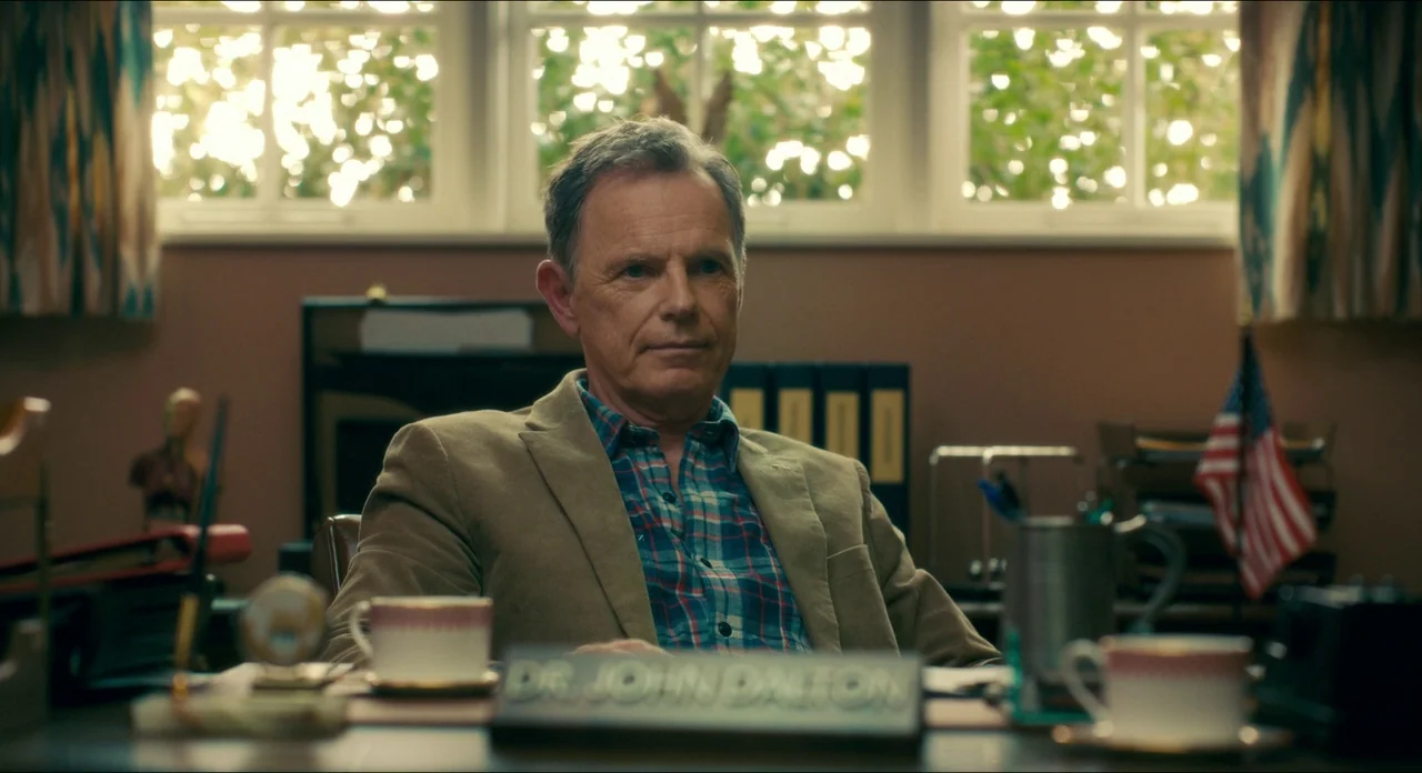 Doctor Sleep movie still: medium — A professional desk workspace features a nameplate for Dr. John Dalton centered on the foreground. A man sits at…