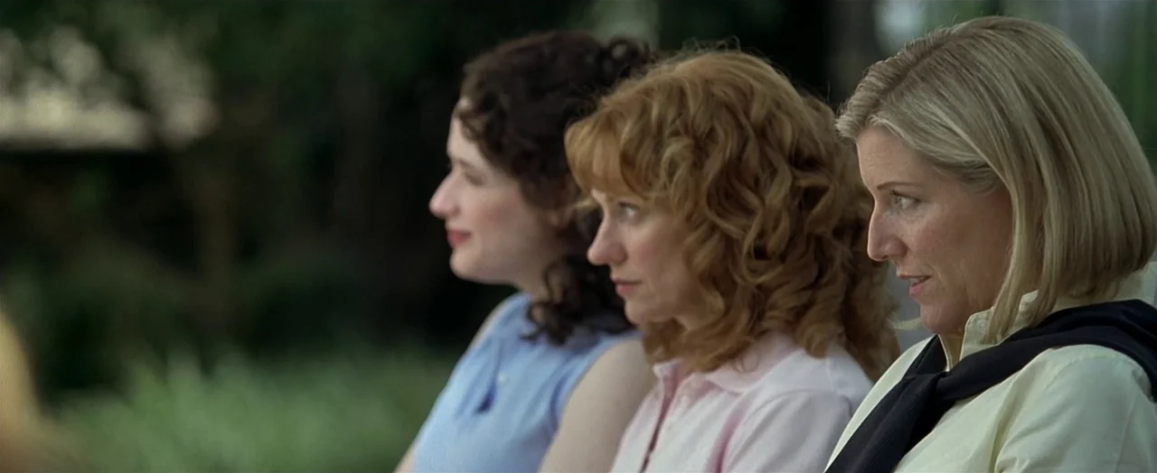 Little Children (2006) movie still: medium — Three women sit side by side in a lush outdoor setting during the day. They appear to be attending an…