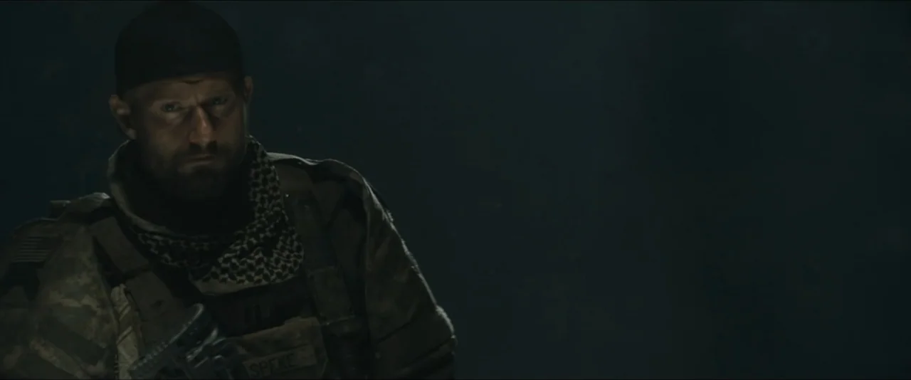 World War Z (2013) movie still: medium — A man wearing tactical military gear stands against a completely dark and featureless background. The…