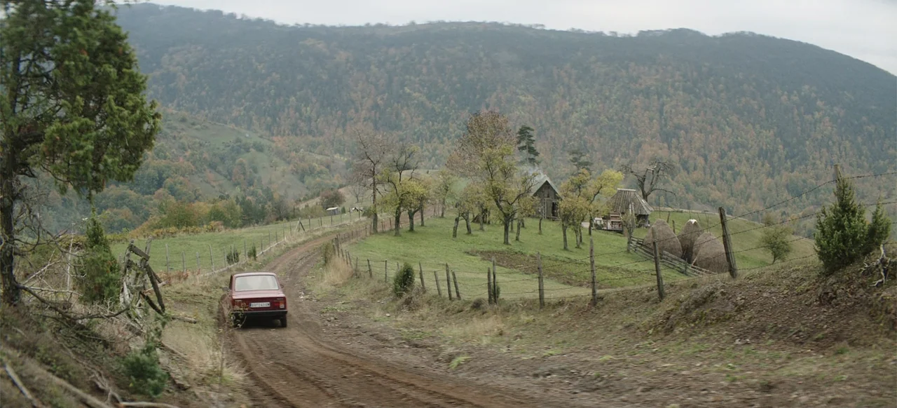 Morir un Poco (1967) movie still: wide — A rural landscape features a dirt road winding through grassy hills with scattered trees. A red car travels…