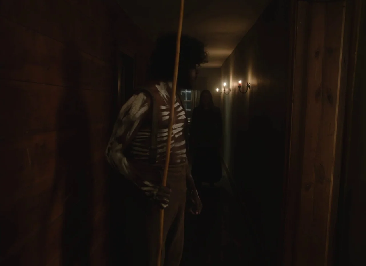 The Nightingale (2018) movie still: medium — A dark, narrow residential hallway features wood-paneled walls and dim electric wall sconces. A man…