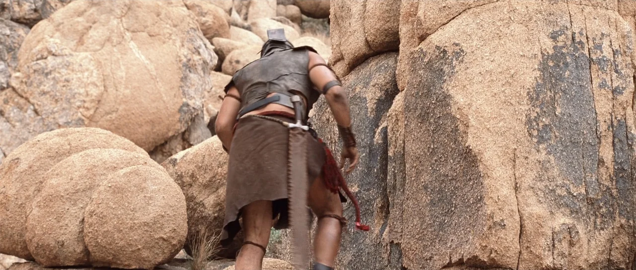 The Scorpion King (2002) movie still: fullbody — A rugged desert landscape covered in large light-brown granite boulders and rock formations. A…