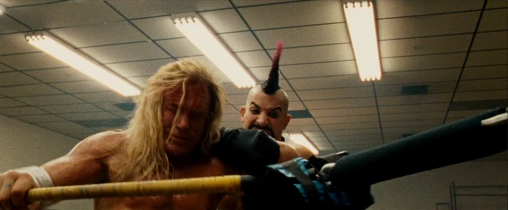 The Wrestler (2008) movie still: medium — A utilitarian room features a white dropped tile ceiling with long recessed fluorescent lights. One man…